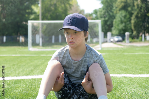 Boy sitting soccer field in summer day. Leisure children with Down syndrome, disability © Elena