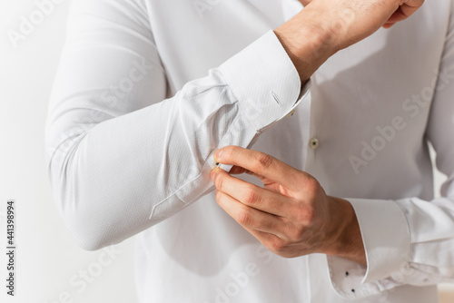 Cropped view of man buttoning sleeve of white shirt photo