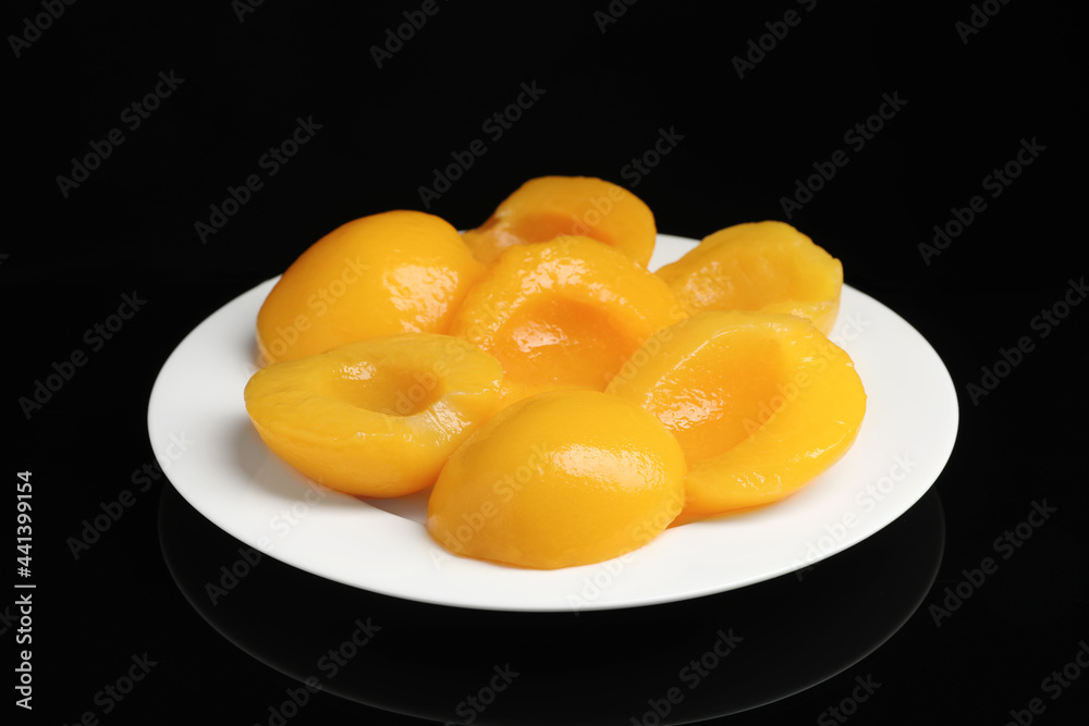 Plate with canned peach halves on black background