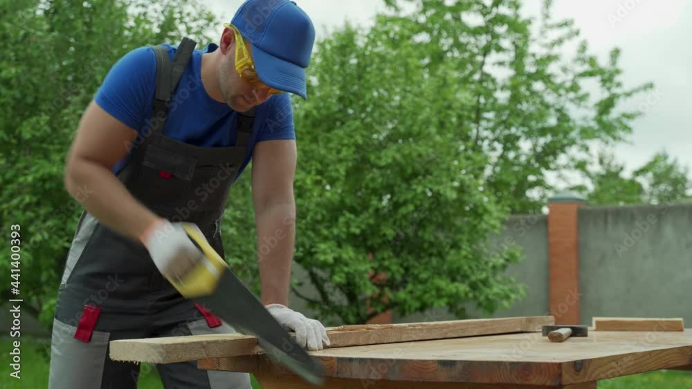 Male carpenter with a saw with protective tools sawing hand saw wood Male carpenter with a saw with protective tools sawing hand saw wood