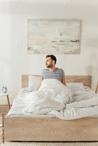 Side view of bearded man sitting on bed at home in morning