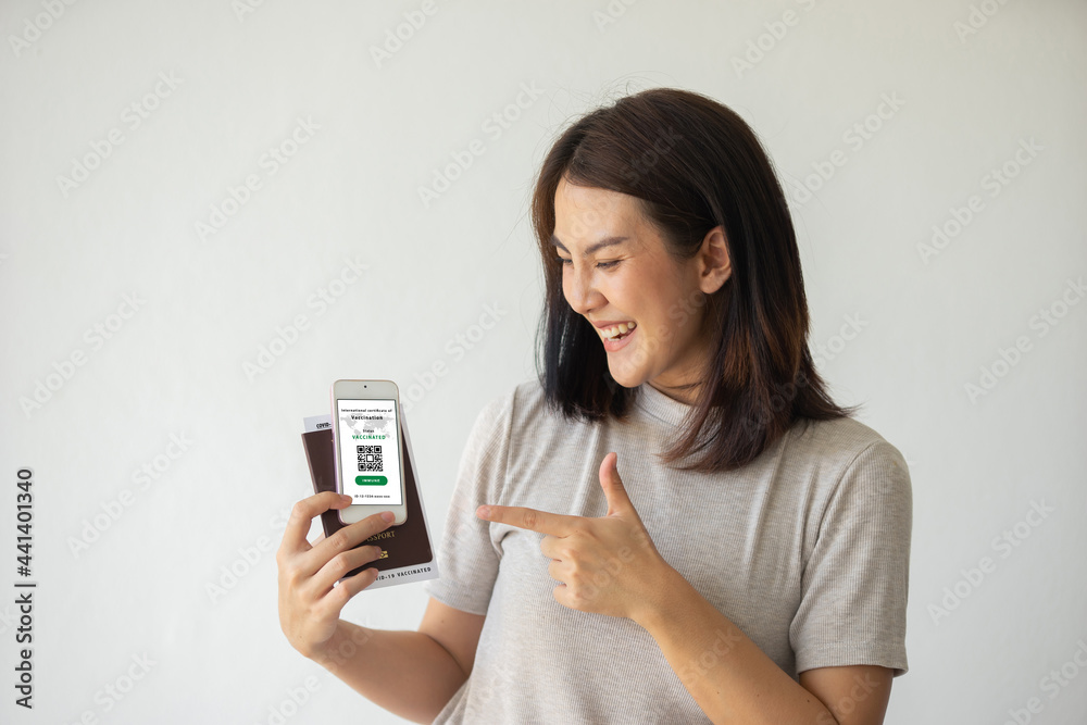 Asian female happy smile holding health passport of vaccination certification on smartphone and passport with vaccination label inside on white background. Travel concept during COVID-19 pandemic. Asian female happy smile holding health passport of vaccination certification on smartphone and passport with vaccination label inside on white background. Travel concept during COVID-19 pandemic.