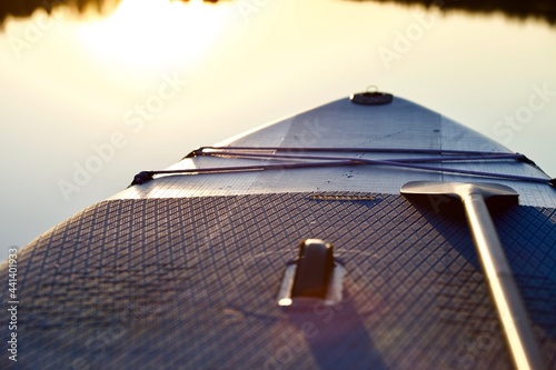 Paddle board and surf board with paddle in sunset light on water background close up. Surfing and SUP boarding equipment in sunset lights close-up. Outdoor water sports. Surfing lifestyle backgrounds.