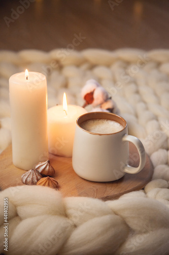 Cup of cappuccino, cookies, and candles on the background of blanket of thick yarn.