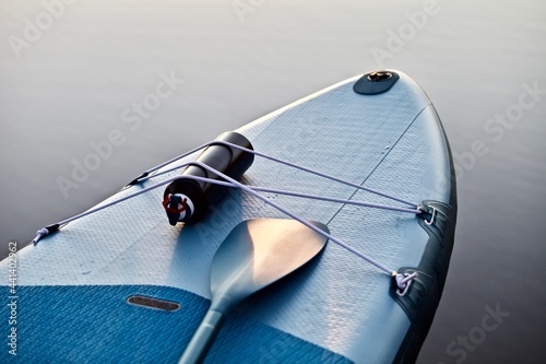 Paddleboard and surf board with paddle on blue water surface background close up. Surfing and SUP boarding equipment in sunset lights close-up. Outdoor water sports. Surfing lifestyle backgrounds. photo