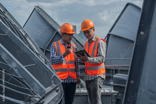 worker on a site. Two Asian engineer discuss job with tablet on cooling tower background. Two worker co-worker on cooling tower.