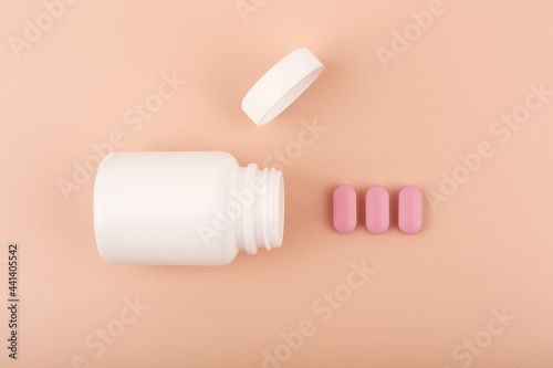 Creative flat lay with white opened medication bottle with pink spilled pills in a row against pastel pink background. Concept of supplements and vitamins for pregnant women