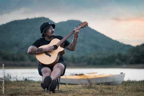Young male play on acoustic guitar in summer fields during a beautiful sunset, Romantic young man playing the guitar on the beach.