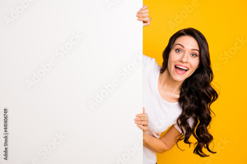 Portrait of attractive cheerful wavy-haired girl holding big board copy empty space offer isolated over bright yellow color background