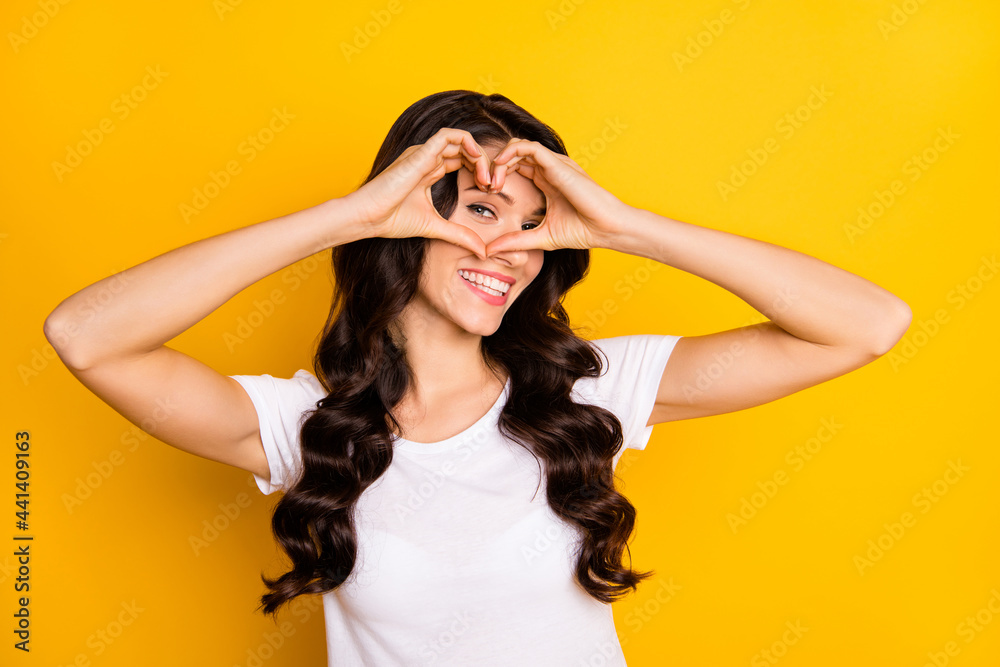 Naklejka premium Portrait of attractive cheerful wavy-haired girl showing heart shape sign isolated over bright yellow color background