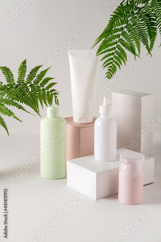 White bottles cosmetic product on white and pink platforms with fern leafs. Exhibition white podiums with cosmetics product.