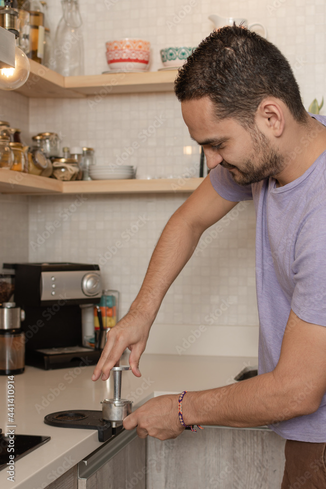 Smiling latin man pressing ground coffee into bottomless portafilter holder using tamper for preparing coffee in his home kitchen. Brewing coffee Smiling latin man pressing ground coffee into bottomless portafilter holder using tamper for preparing coffee in his home kitchen. Brewing coffee