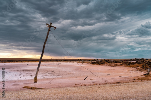 An old power pole leaning over on the edge of a salt lake under a gloomy sky