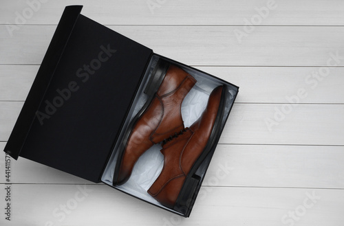 Pair of stylish leather shoes in black box on white wooden background, top view photo
