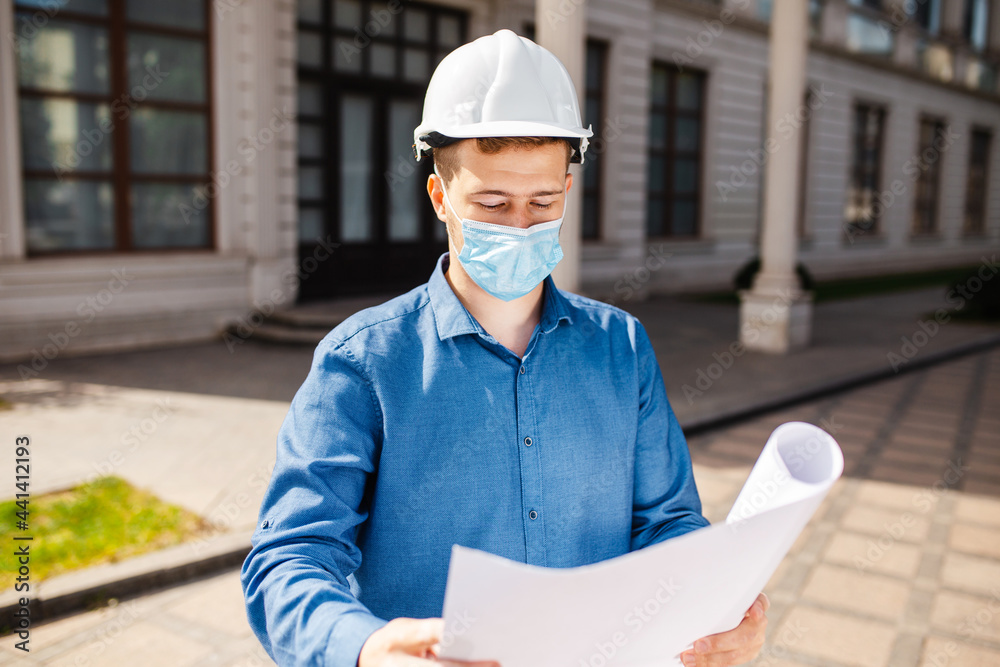 Portrait of an architect builder in protective mask and helmet studying layout plan of the object. Architect looking at blueprints in a building site. Portrait of an architect builder in protective mask and helmet studying layout plan of the object. Architect looking at blueprints in a building site.
