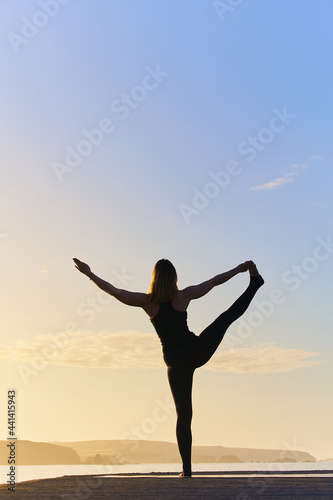 yoga training and meditating on pose on the beach at dawn or dusk. Woman yoga exercising training in serene ocean landscape. Silhouette as a woman against the sun.