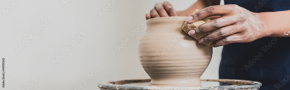 partial view of young african american woman modeling wet clay pot on wheel with sponge in pottery, banner - obrazy, fototapety, plakaty 