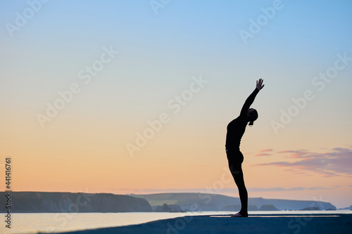 woman doing yoga asanas by the sea in a nice sunrise