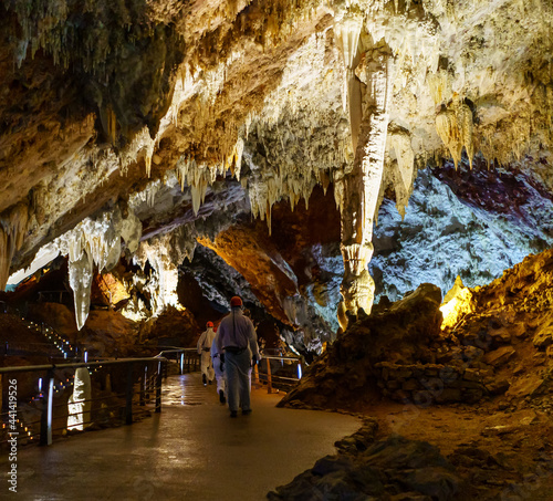 People dressed in white overalls exploring a huge cave of stalactites.