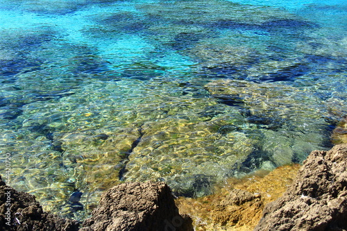 Stones on the seashore in Mallorca are beautifully visible under water in sunny weather, yellow, blue and dark blue colors of the water, water ripples, summer, sunny