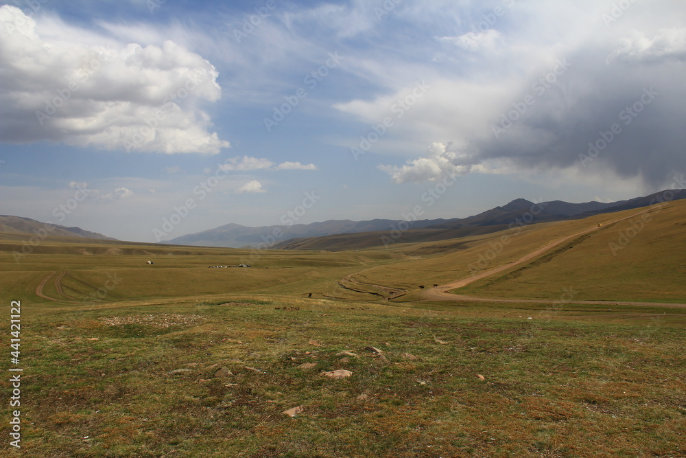 A wide steppe space on the Assy plateau with roads and green hills, mountain ranges are visible in the distance, a sky with beautiful expressive clouds, summer, sunny A wide steppe space on the Assy plateau with roads and green hills, mountain ranges are visible in the distance, a sky with beautiful expressive clouds, summer, sunny