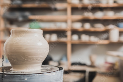 Fotografija wet clay pot on pottery wheel on wooden bench in art studio