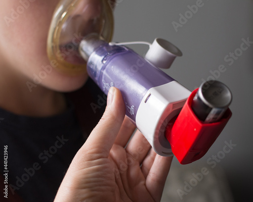 Slika na platnu Young boy using asthma inhaler with help from parent; a spacer is used to help c