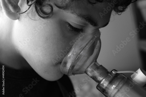 Young boy taking asthma inhaler medication using a spacer and mask photo