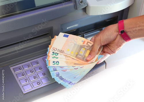 hand with banknotes just picked up from the ATM and the numeric keypad for entering the PIN