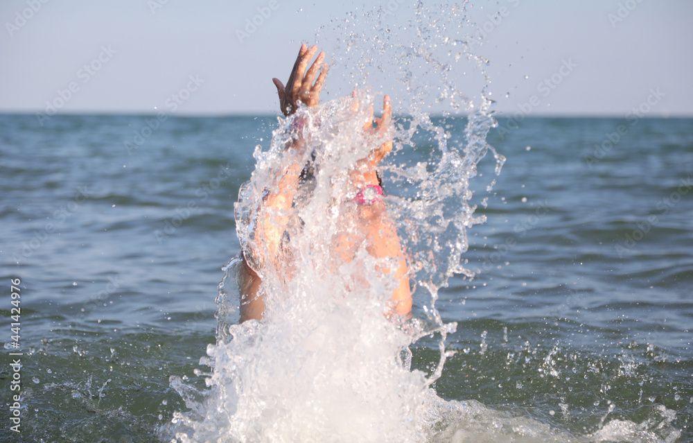 young girl splashes the sea water playing and having fun during the summer vacation