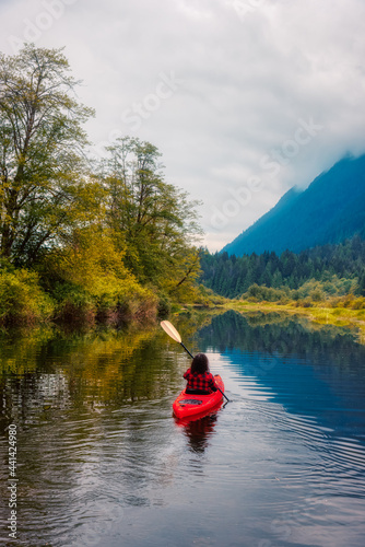 Adventure Caucasian Adult Woman Kayaking in Red Kayak surrounded by Canadian Mountain Landscape. Artistic Color Render. Taken in Widgeon Valley, Pitt Meadows, Vancouver, British Columbia, Canada.