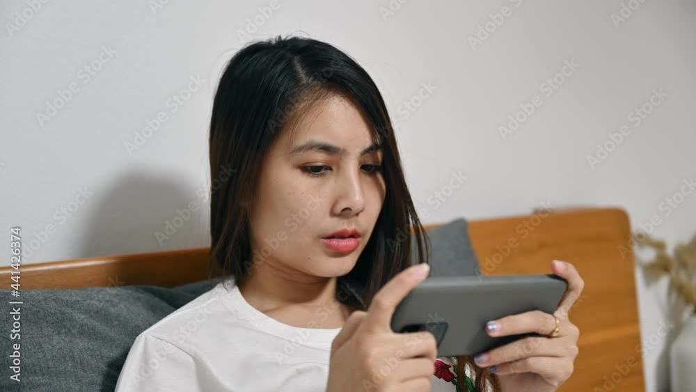 Serious young asian woman playing game online with mobile phone on bedtime Serious young asian woman playing game online with mobile phone on bedtime