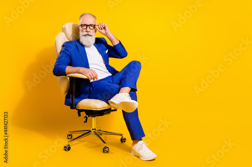 Portrait of attractive imposing serious man sitting in chair touching specs isolated over bright yellow color background photo