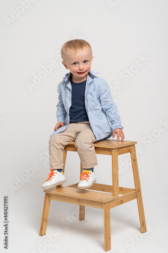Little boy on the white background making funny face - blonde caucasian child sitting on the wooden ladder