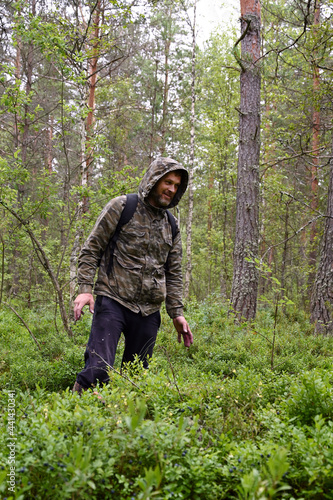 man in camouflage clothing with a backpack in the woods. A forester walks along a path through a dense forest