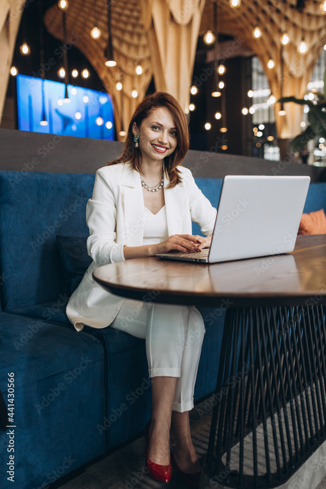 Beautiful Young Freelancer Woman Using Laptop Computer Sitting At Cafe Table. Happy Smiling Girl Working Online Or Studying And Learning While Using Notebook. Freelance Work, Business People Concept