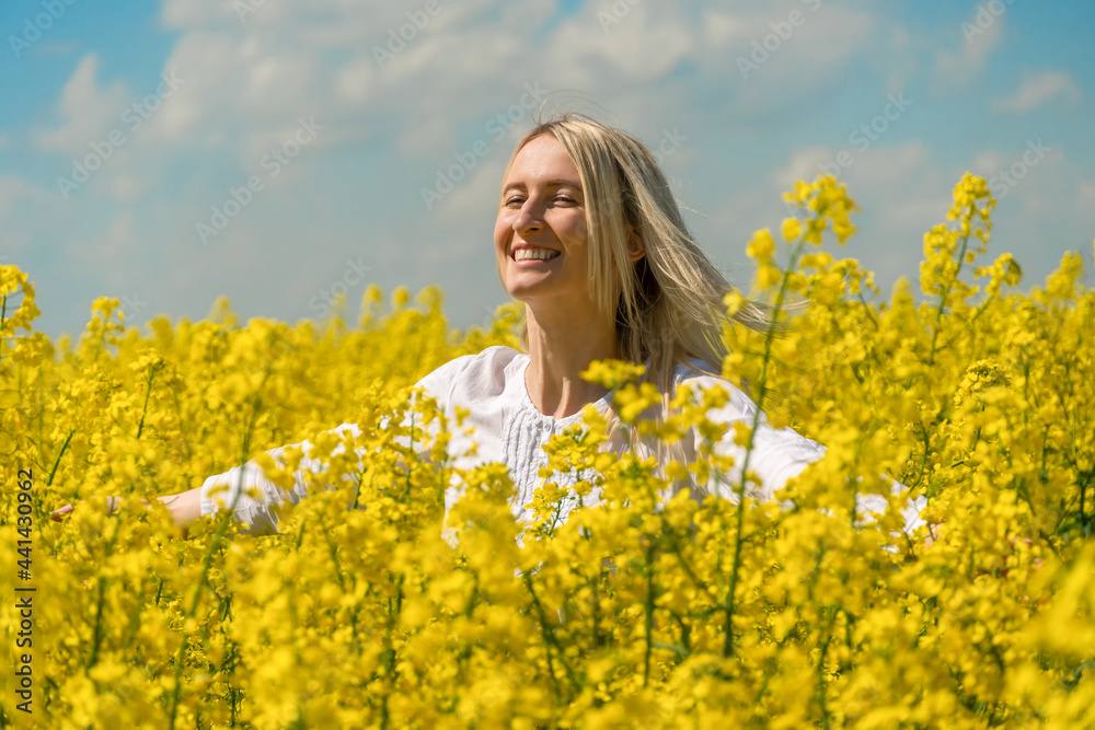 Happy smiling young blonde woman in a white shirt in a rapeseed field with her arms spread out to the side on a sunny day Happy smiling young blonde woman in a white shirt in a rapeseed field with her arms spread out to the side on a sunny day