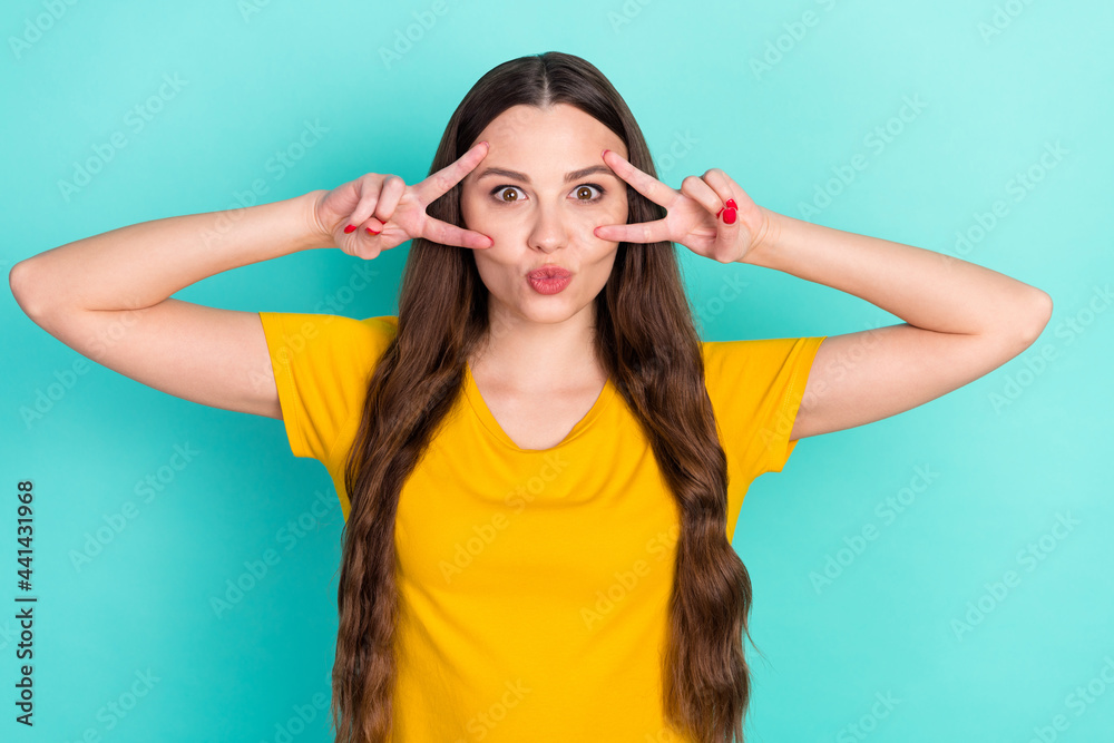 Photo of cute sweet young woman dressed yellow clothes showing v-sign cover eyes pouted lips isolated teal color background Photo of cute sweet young woman dressed yellow clothes showing v-sign cover eyes pouted lips isolated teal color background