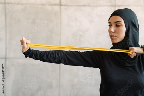 Young muslim woman in hijab doing exercise with expander stretch tape