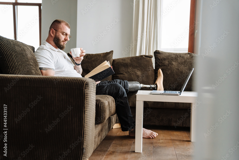 White man with prosthesis reading book while siting on couch at home