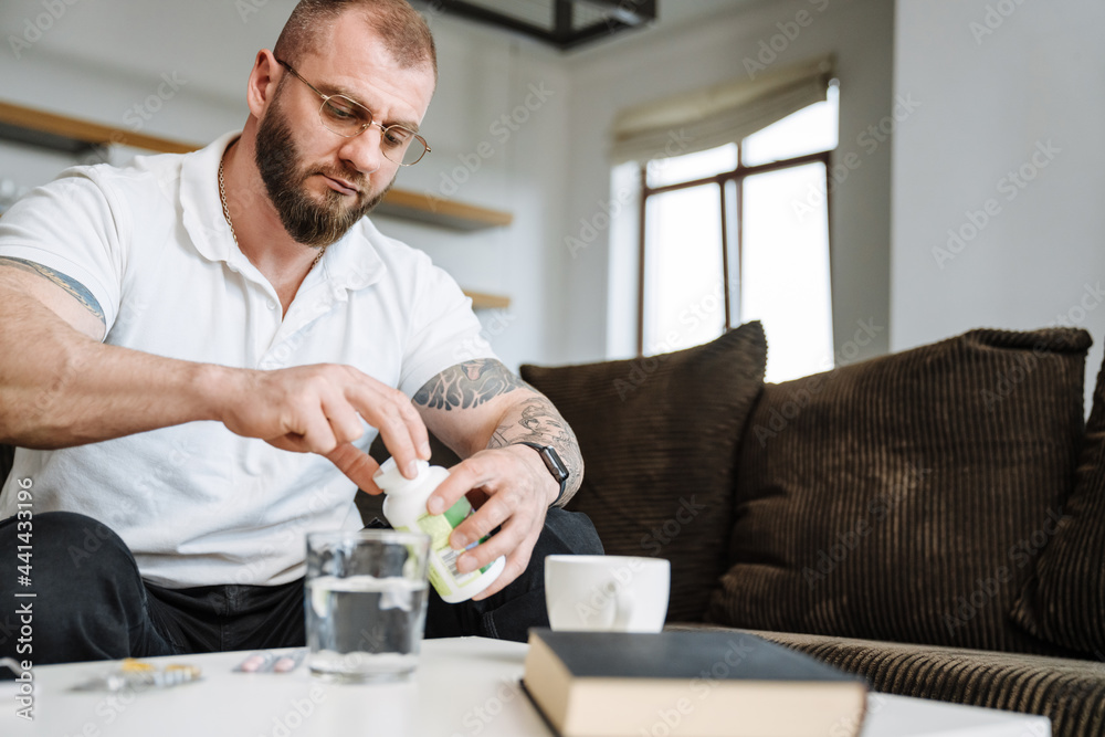 White bearded man taking his medicine while siting on couch at home White bearded man taking his medicine while siting on couch at home