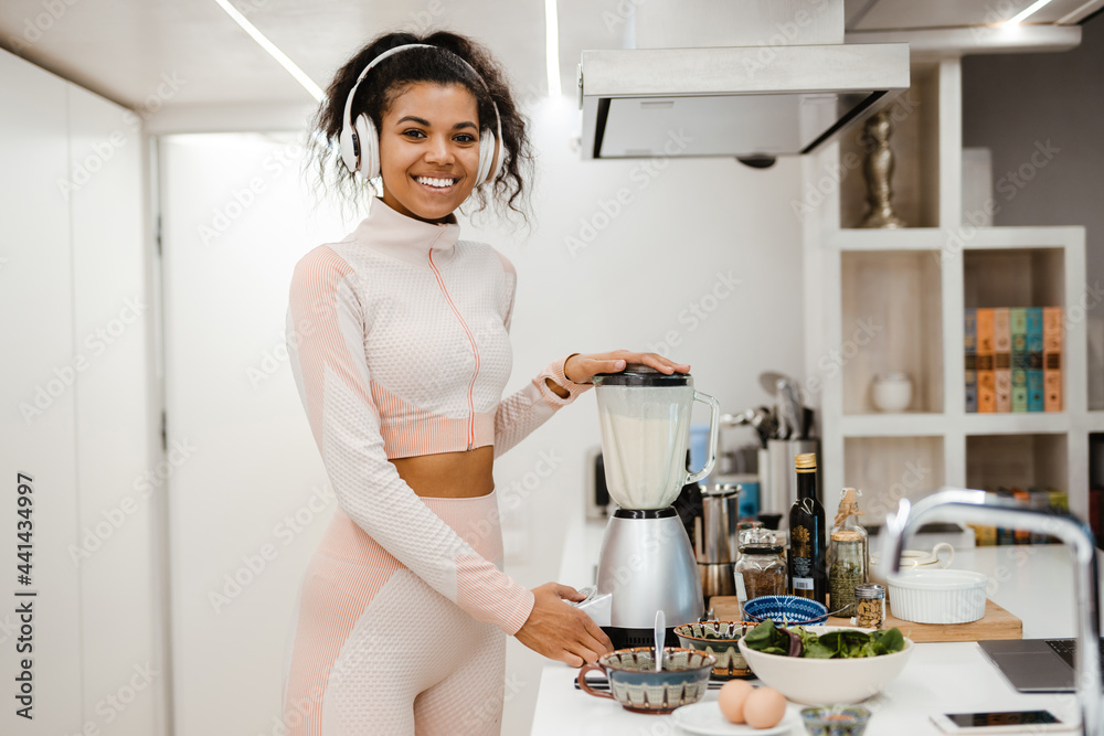 Black woman in headphones smiling and making smoothie at home Black woman in headphones smiling and making smoothie at home