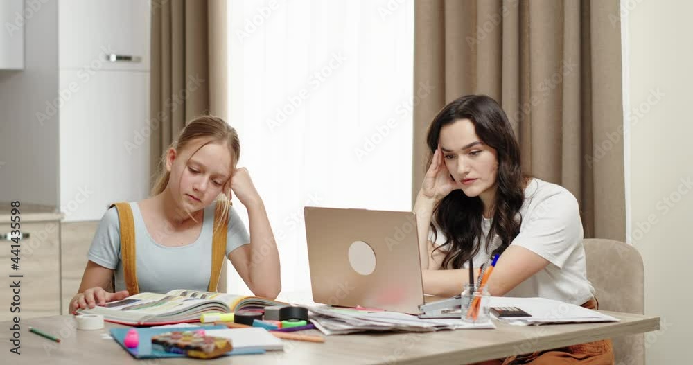 Working mom is busy working sitting at a laptop at home daughter is sitting studying wants attention from mom asks mom to look. Mom ignores her daughter because of work Working mom is busy working sitting at a laptop at home daughter is sitting studying wants attention from mom asks mom to look. Mom ignores her daughter because of work