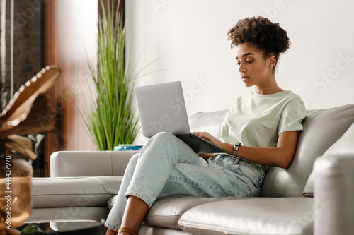 Young black woman working with laptop while sitting on couch at home