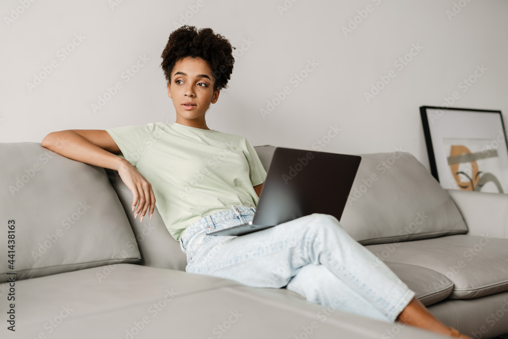 Young black woman working with laptop while sitting on couch at home Young black woman working with laptop while sitting on couch at home