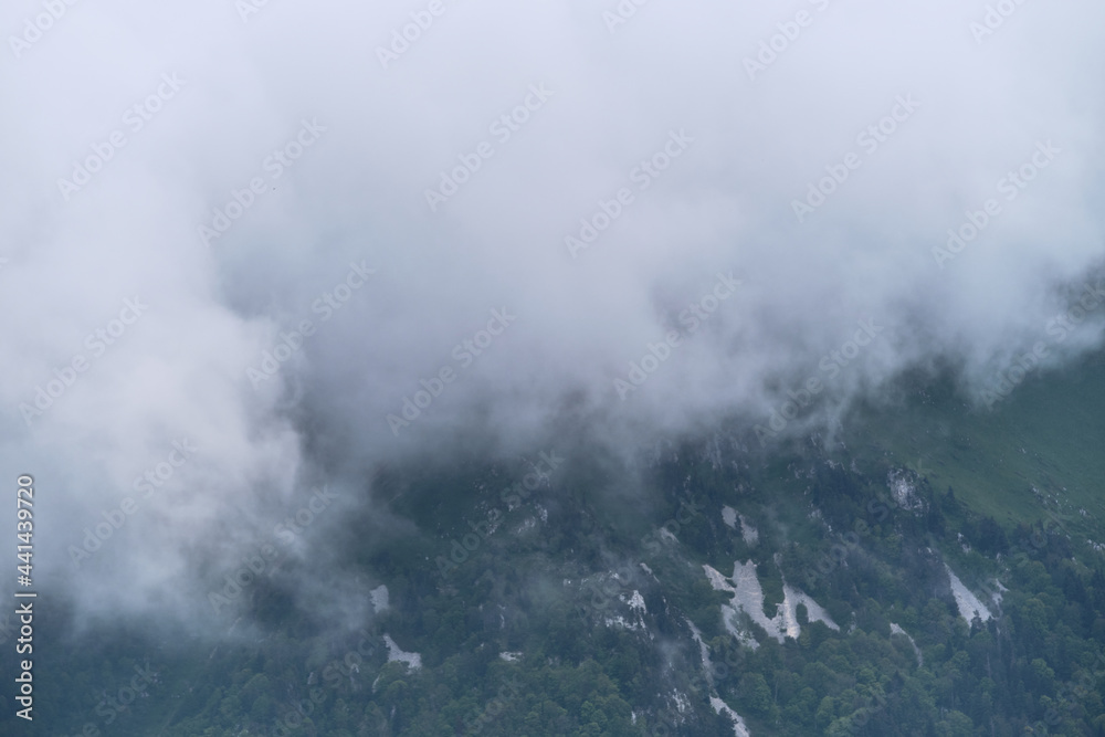 Forest and mountains in fog in cloudy weather. Beautiful landscape of National Park of Russia. Dark thundercloud envelops green mountain peak with coniferous forest.