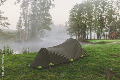 Single green tent in forest near river in the foggy morning