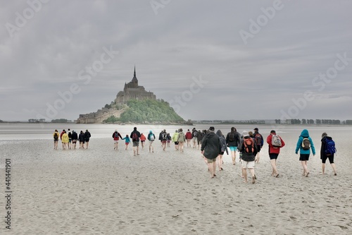 Canvastavla a large group of people walking toward mont saint michel in the bay at low tide