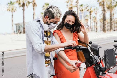 Photography Young people renting electric bike using mobile phone app while wearing safety m