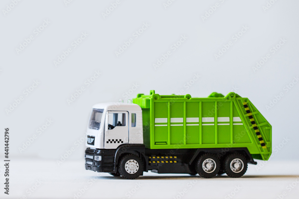 Green garbage truck on the background of a white wall.